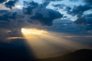 The bright rays of the sun are shining from saturated clouds to mountain range before sunset.