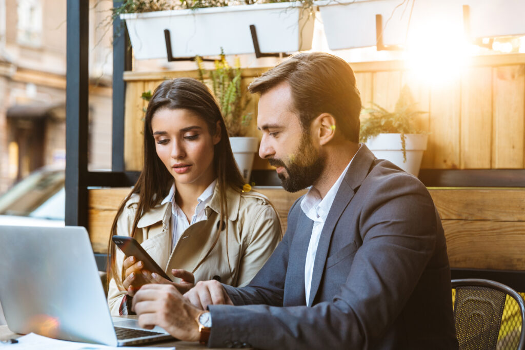 Portrait of successful business couple man and woman in formal wear having conversation and working on laptop together while sitting in cafe outdoors