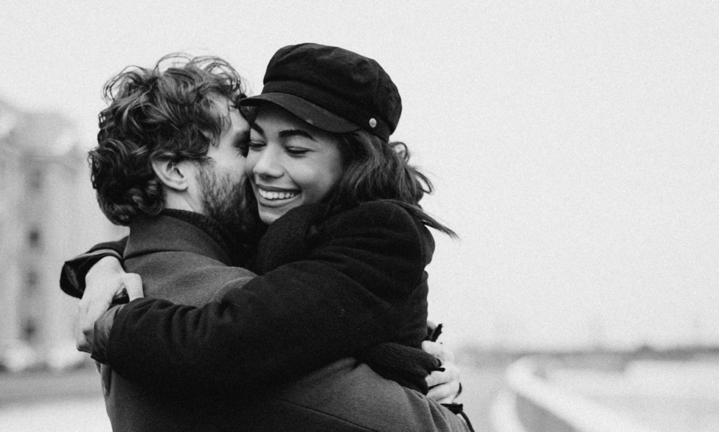 a black woman and white man hugging tightly, the city. skylight is the background.