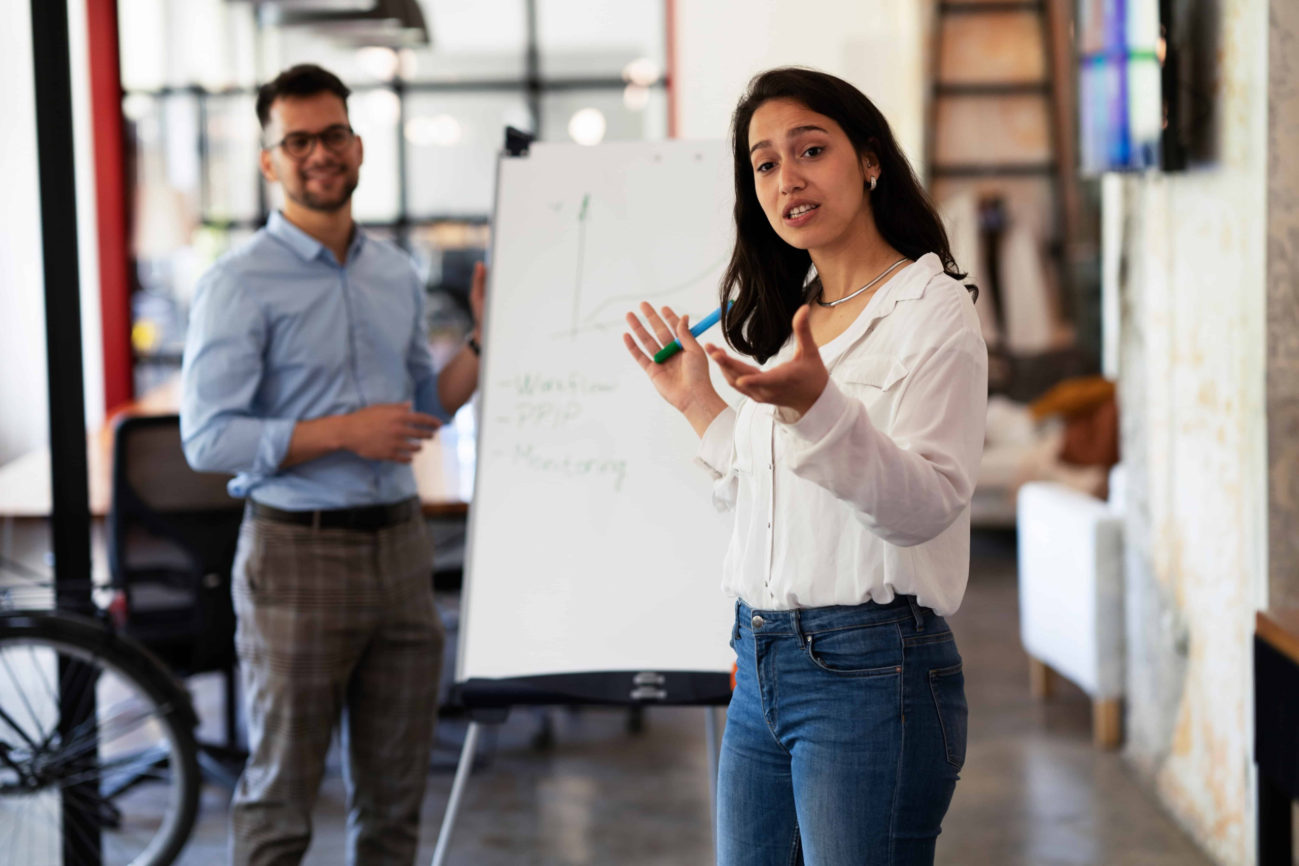 A couple at work, the men is standing at the white board paying attention to what his wife is saying.