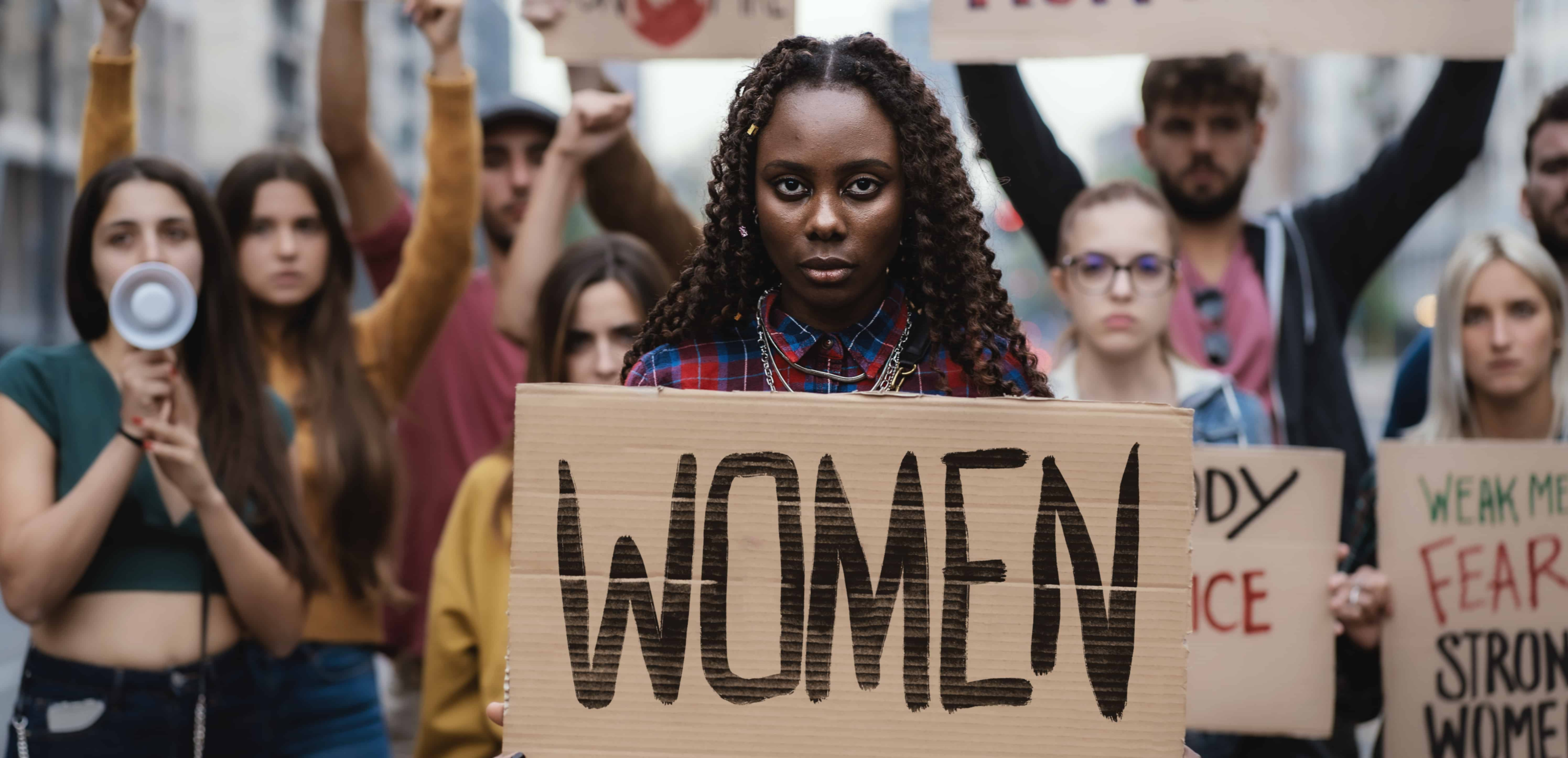 Group of women standing together protesting holding signs that say women!