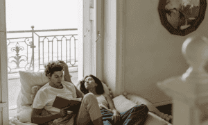 A couple sitting on the bed reading a book to each other