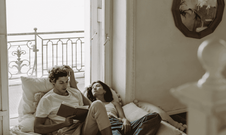A couple sitting on the bed reading a book to each other