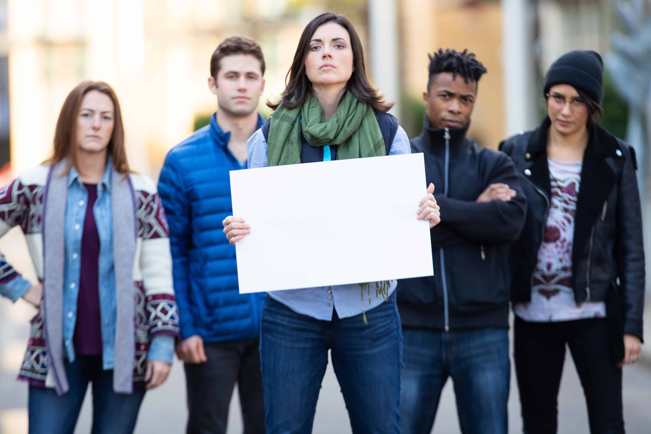 Group of men and women standing together holding up a sign