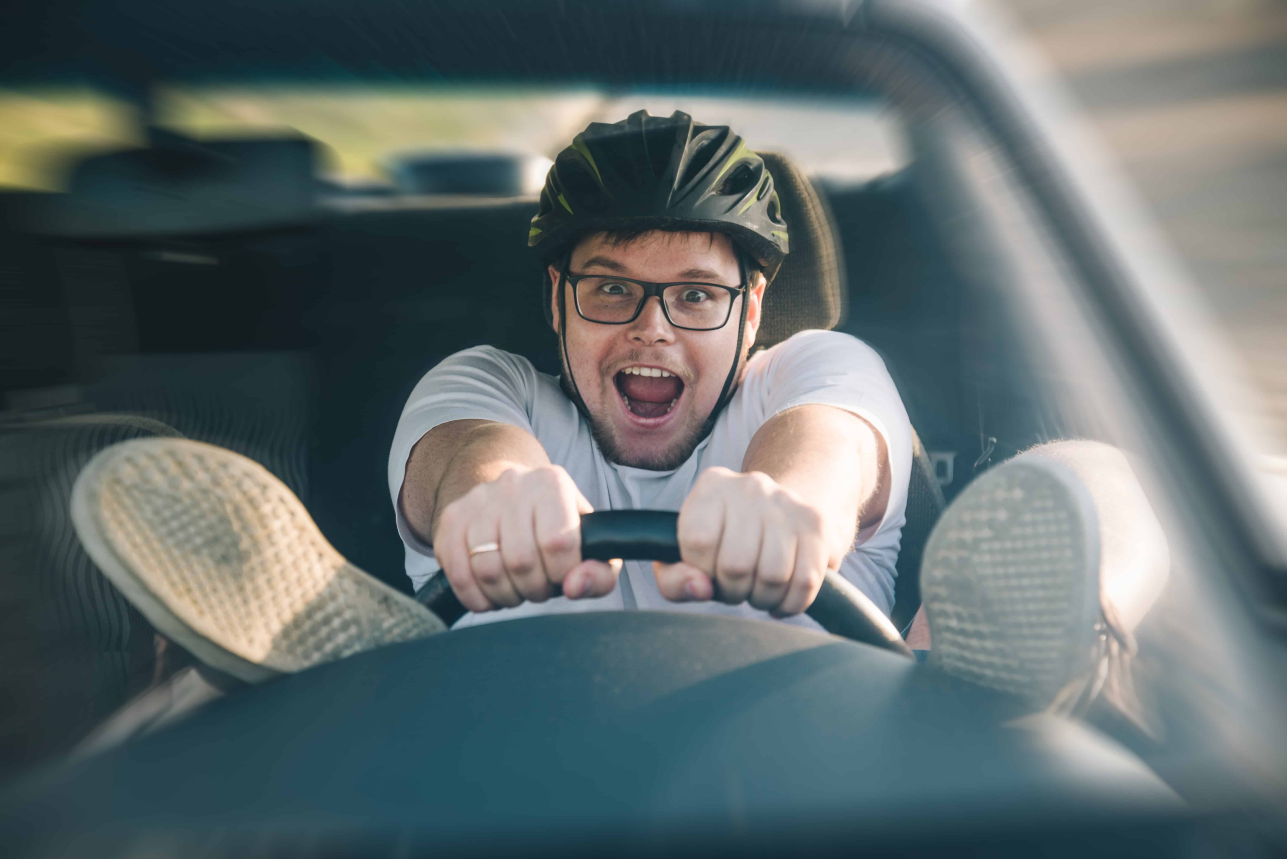A young men driving a car with his feet on the dashboard. He also has a helmet on, more than likely because he is speeding.