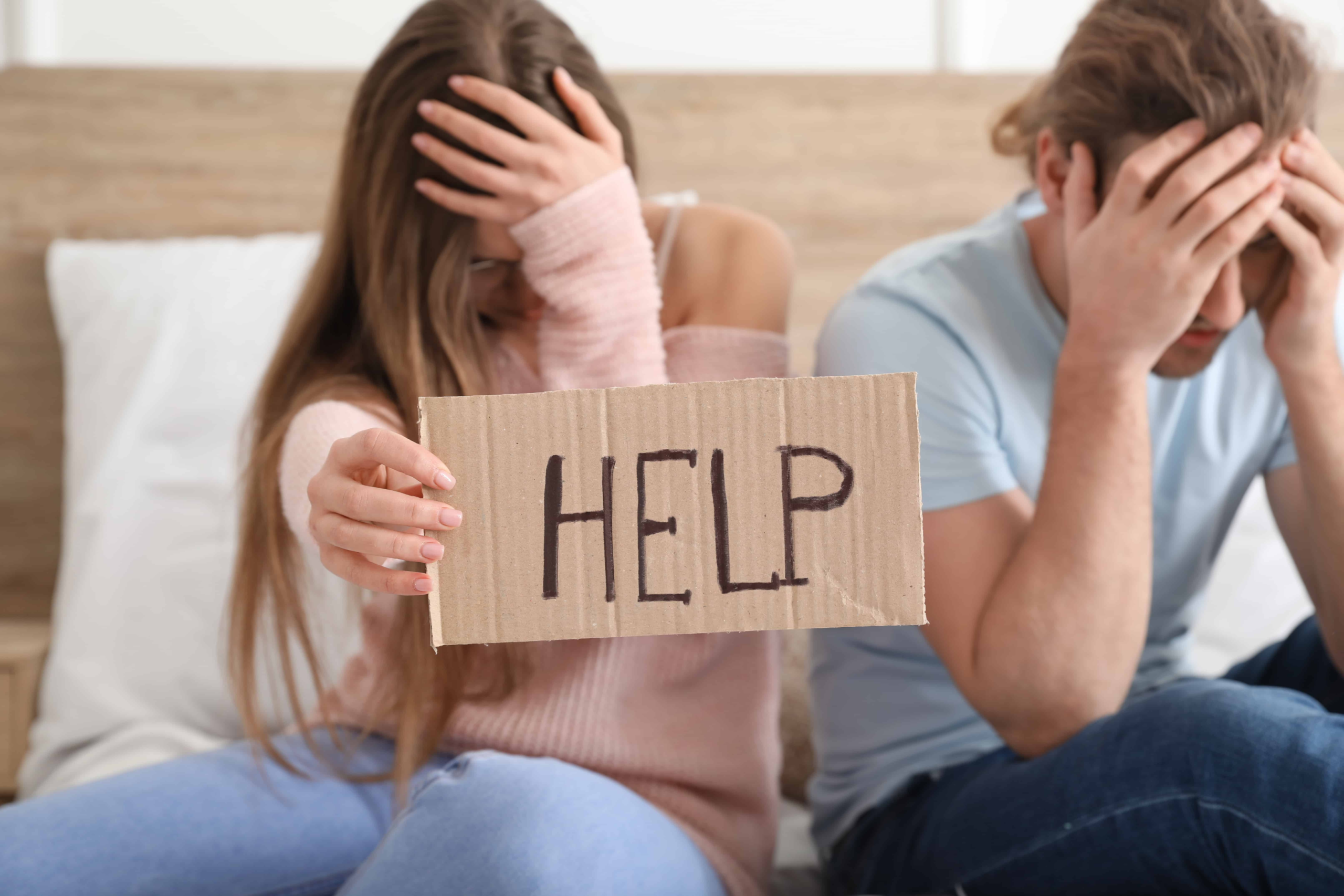 A couple in bed avoiding physical contact holding up a sign that says help. The woman wants help dealing with her partner's fear of intimacy.