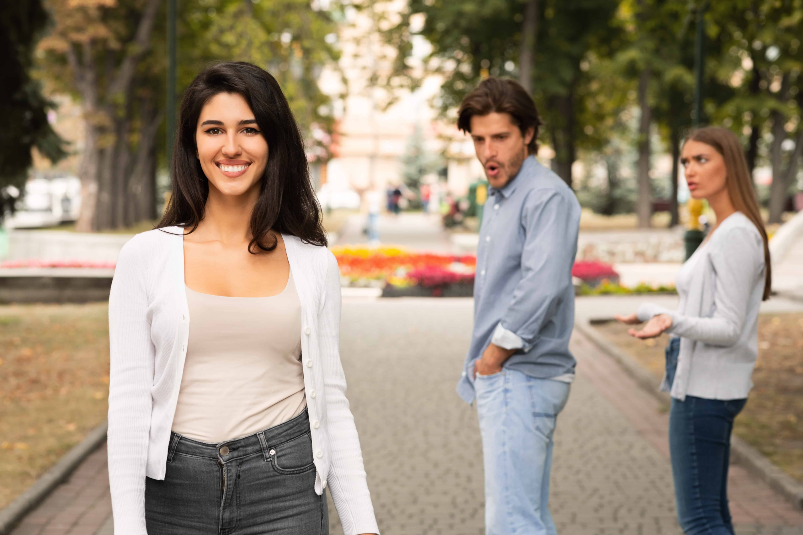 Attractive couple walking down the street while a beautiful woman passes by. The man completely stops to look at the woman. His girlfriend is not happy at the scenario.