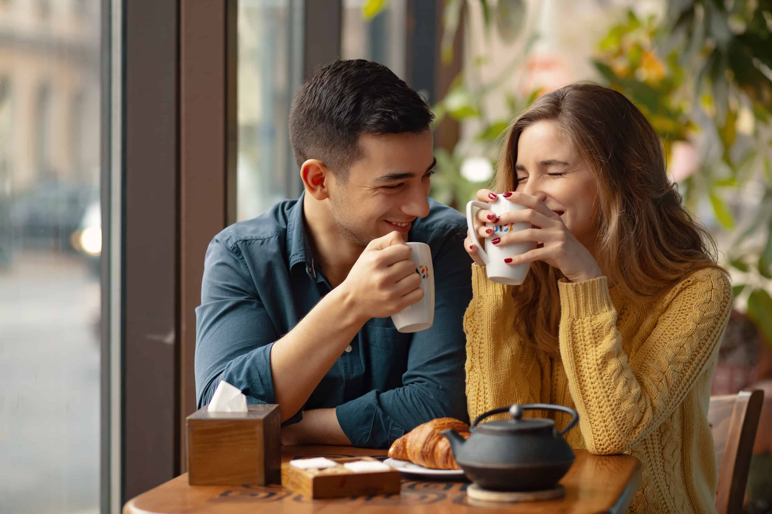 Best friends sitting in a coffee shop talking about each other's interests, laughing and drinking coffee together.