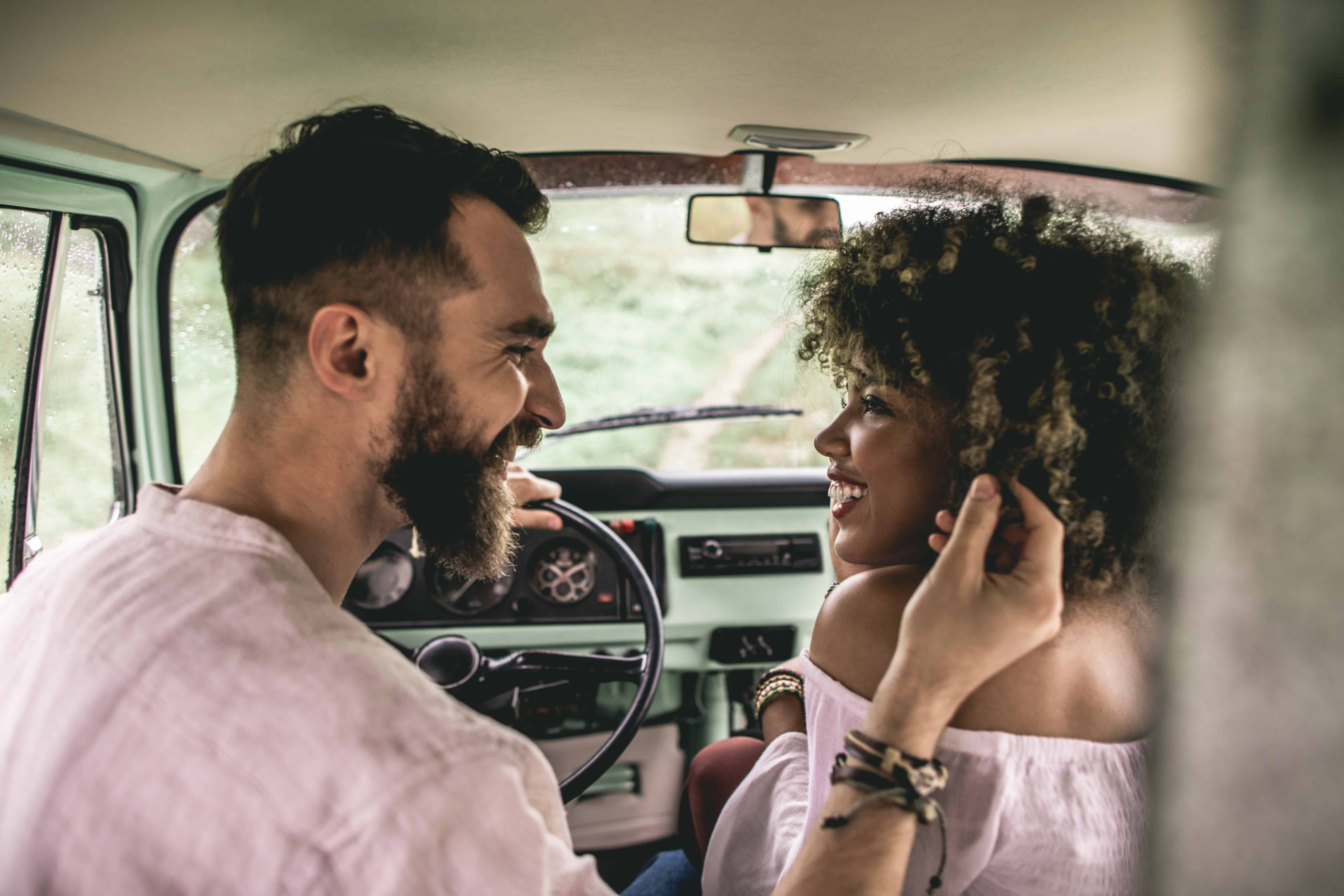 An interracial couple sitting in the car together getting ready to kiss.