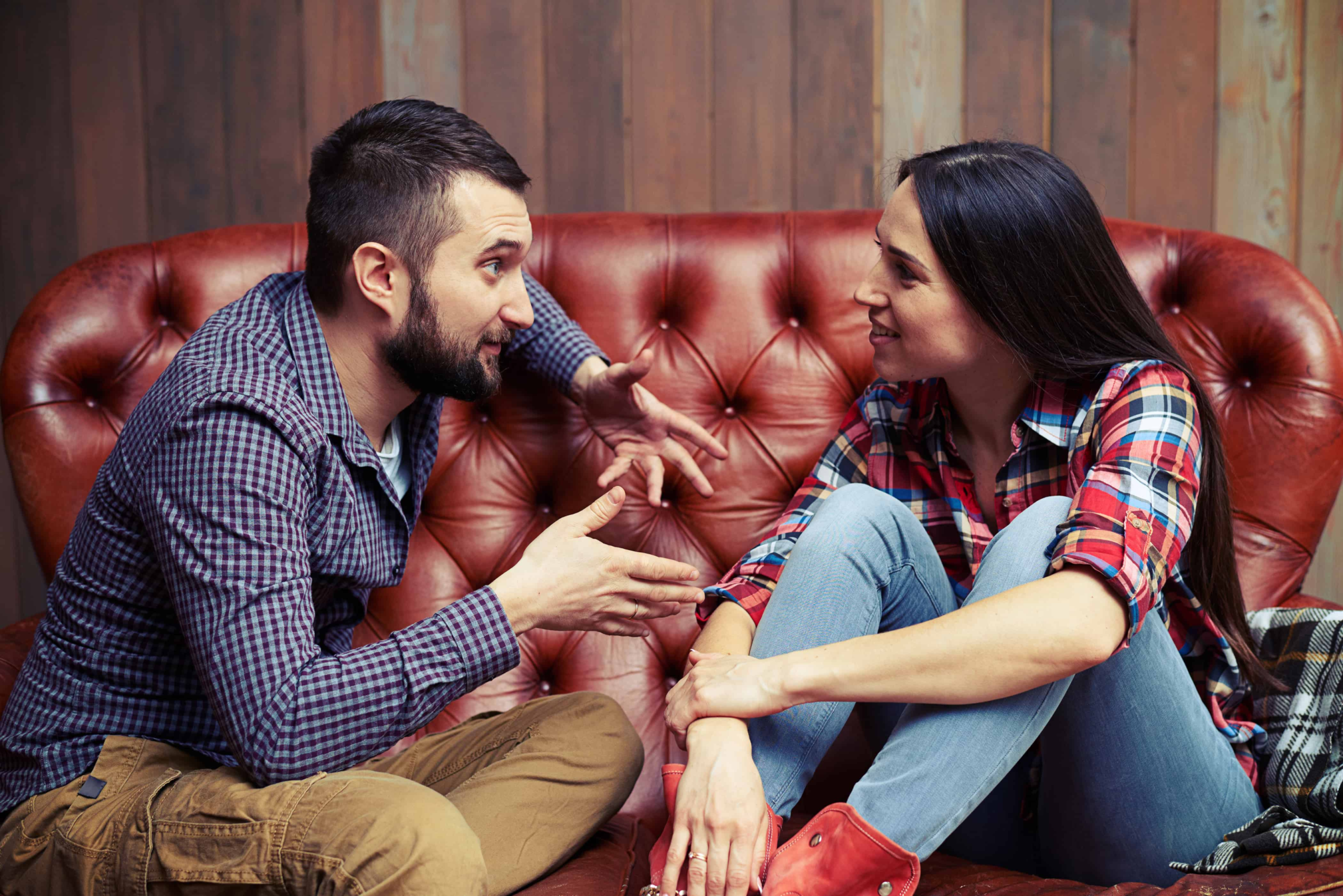 An attractive couple sitting on the couch having a conversation. Both parties are very interested in what the other has to say.