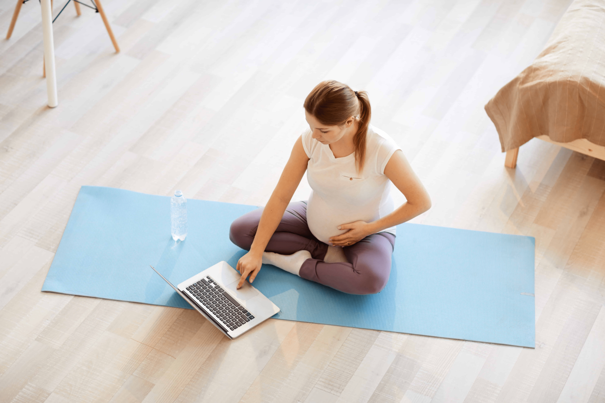 A pregnant mom sitting and doing yoga while she watches the instructor on her yoga mat in the comfort of her home.
