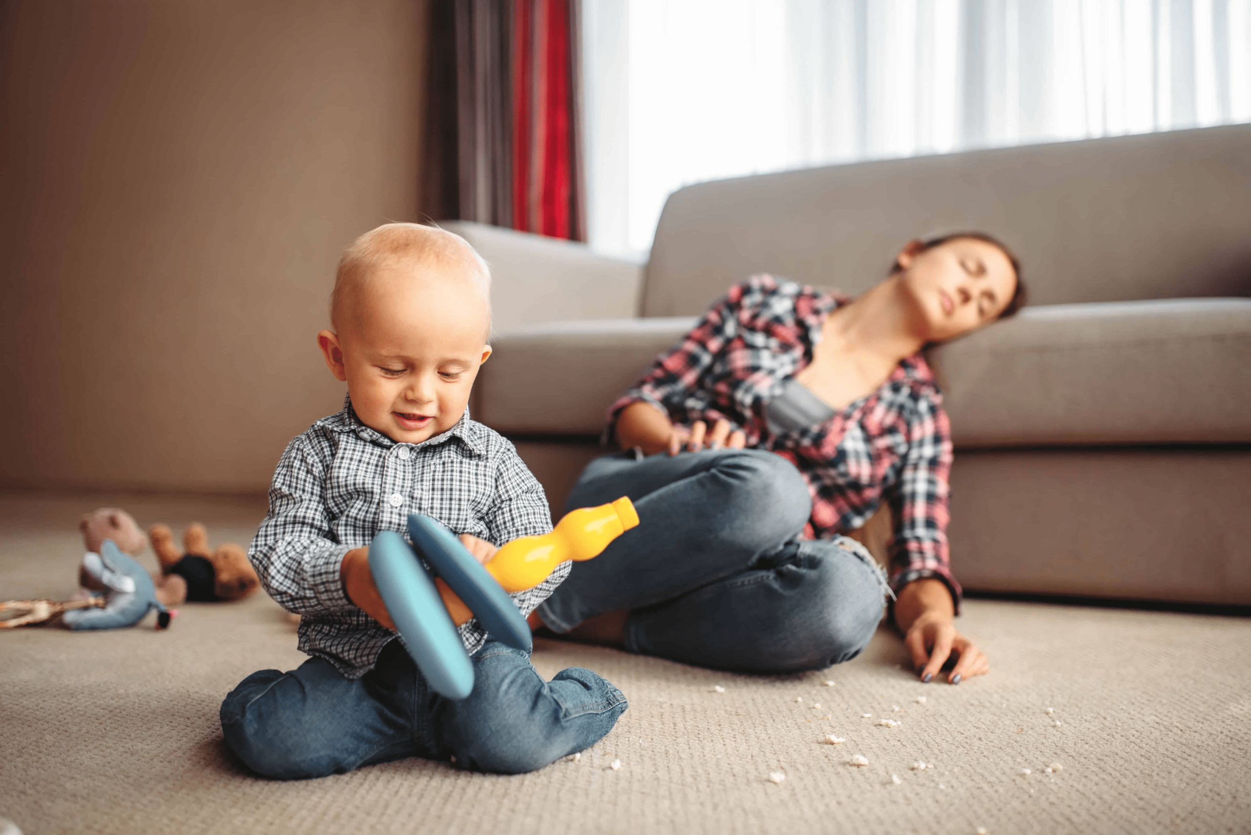 A woman sitting in her living room passed out. The living room is very dirty and her toddler is in there playing with toys all by himself.