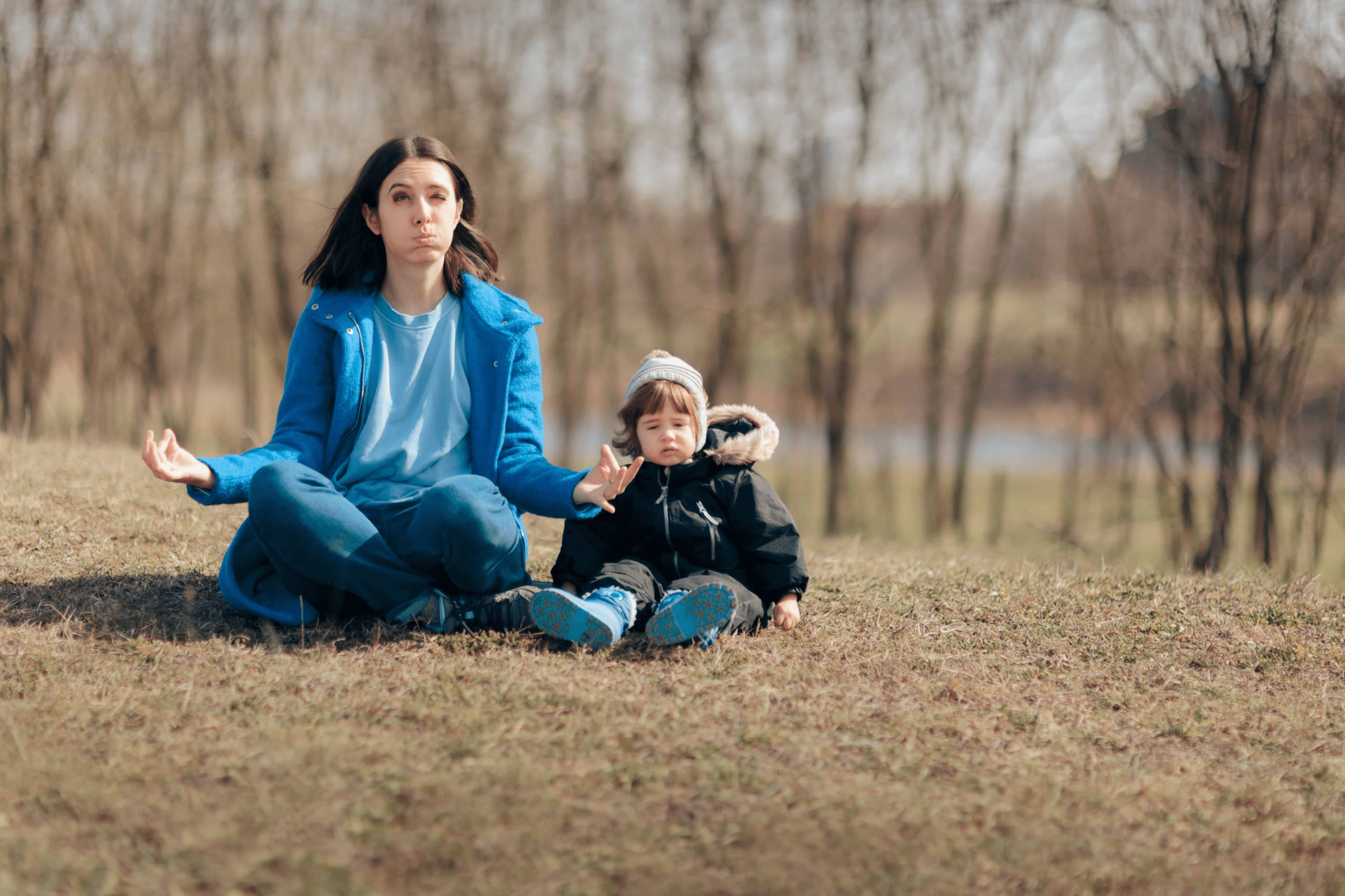 A woman sitting in a grassy area with her child breathing. The child is just sitting while the mom looks a little stressed.