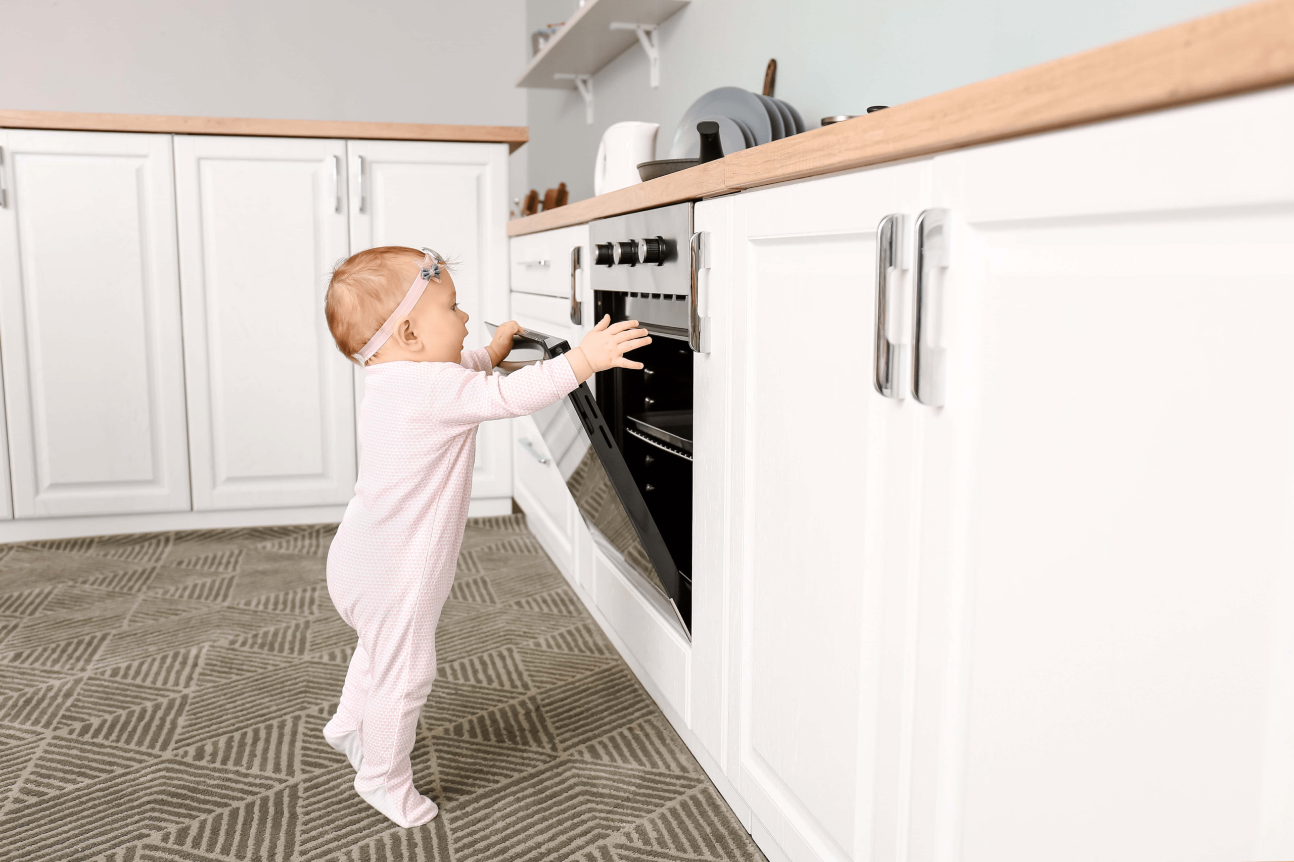 Baby standing in the kitchen opening the oven playing with all the knobs.