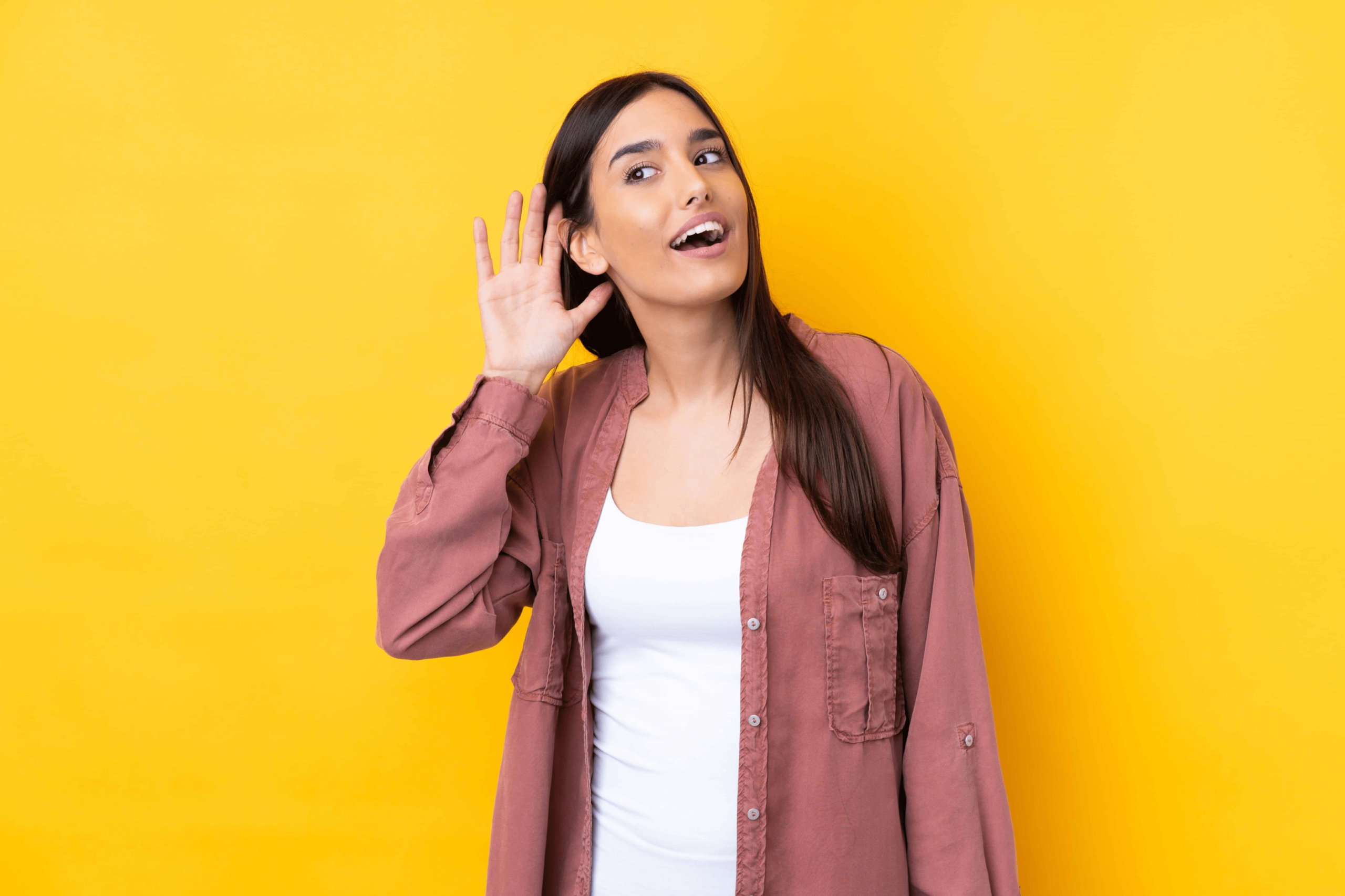 A woman holding her hand up to her ear; imitating the act of listening.