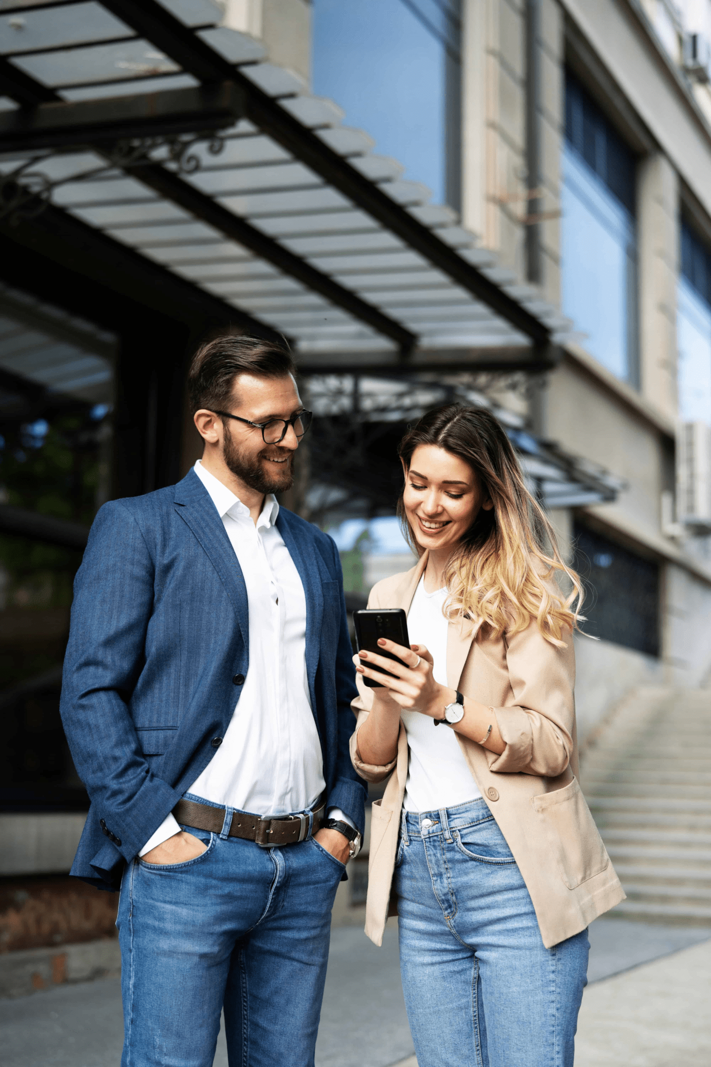 A man and a woman outside. The woman has her phone out and is showing the guy something.