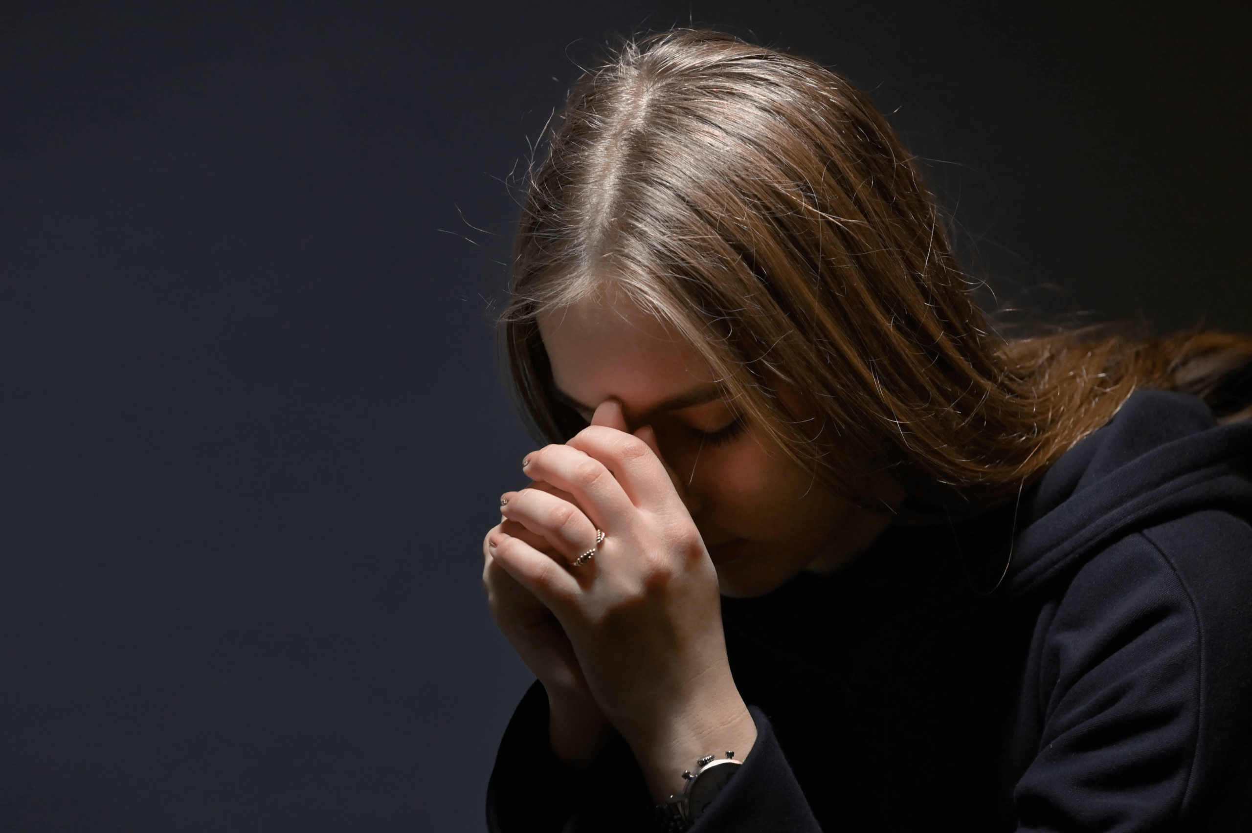 A woman with her head down and holding her hands together to pray.