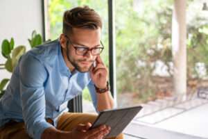 Man in the kitchen relaxed on a chair with tablet, online streaming with internet and reading ebook or watching film at home. Happy male person with technology, subscription and mobile app with break in kitchen.