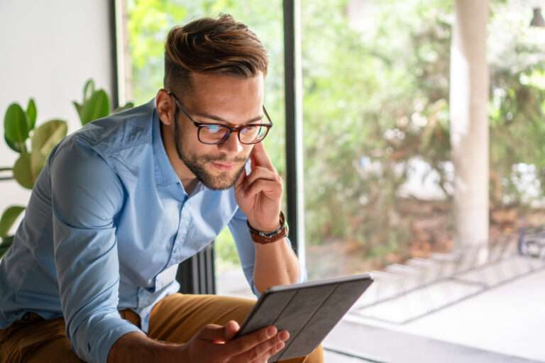 Man in the kitchen relaxed on a chair with tablet, online streaming with internet and reading ebook or watching film at home. Happy male person with technology, subscription and mobile app with break in kitchen.