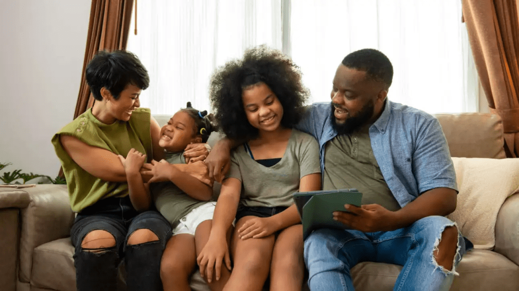 A black family all sitting together having a good time all watching an iPad together.