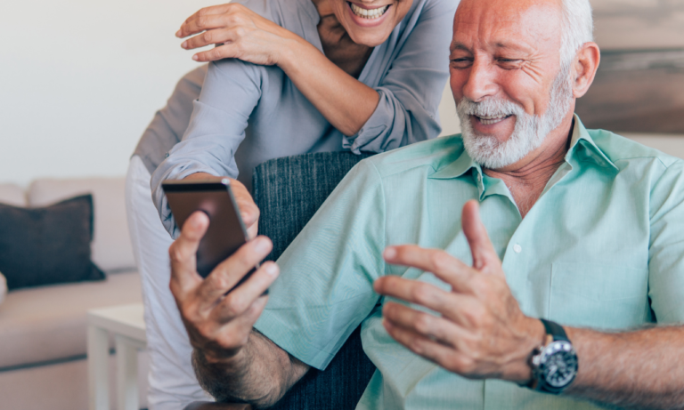 a couple together, the man looks at his phone while the woman is peering over his should. they are laughing and having a great time.