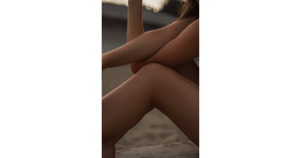 A woman sitting on the beach giving herself a hug and some quality time.