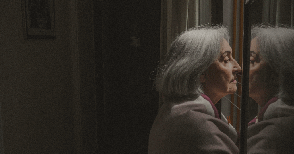 An older woman staring out of the window looking a little lost as if she is thinking about heavy things/ topics