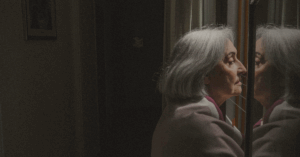 An older woman staring out of the window looking a little lost as if she is thinking about heavy things/ topics