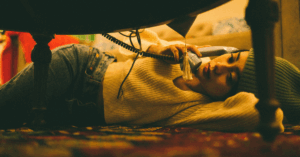 It is a woman laying on the ground holding the phone to her ear. She is also wearing a hat and looks pretty out of it.