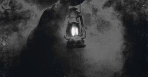 A person walking inn pitch blackness holdinng a light up attempting to see what's in front of them.